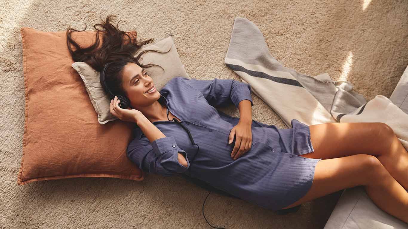 Une femme est allongée sur le sol avec un coussin et écoute de la musique avec des écouteurs.